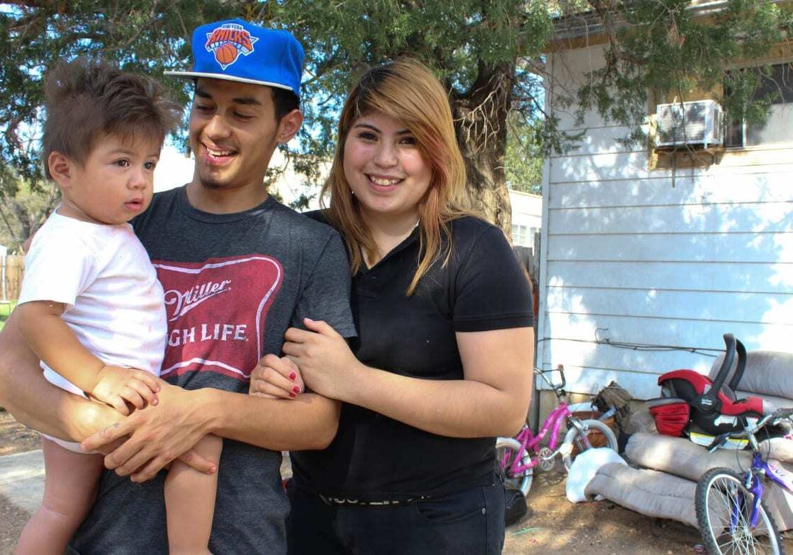 Claudia Rivera (right) and her boyfriend, Jesùs Varela, stand in the yard of their Liberal, Kansas, home with their 1-year-old son, Fabian. (Photo: Esther Honig | Heartland Health Monitor)