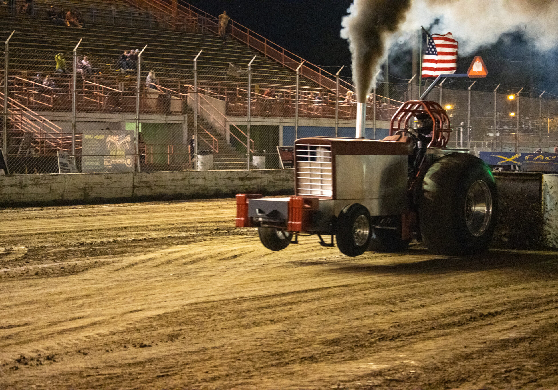A tractor spews mud up as it drags a weighted sled across the mud.