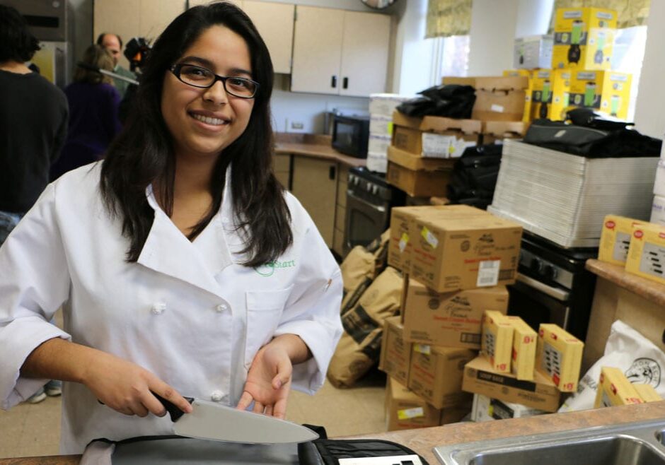 teen girl in white chef's coat poses wilth chef's knife.