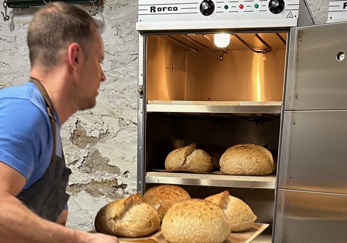 Jon Szajnuk pulls sourdough bread loaves from his oven.