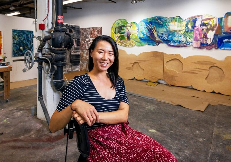 Artist Kathy Liao in her downtown studio with a draft (top right) of her artwork for the new KCI terminal. Titled, “Hello and Goodbye,” the piece will feature acrylic on birchwood panels and ceramic tiles.