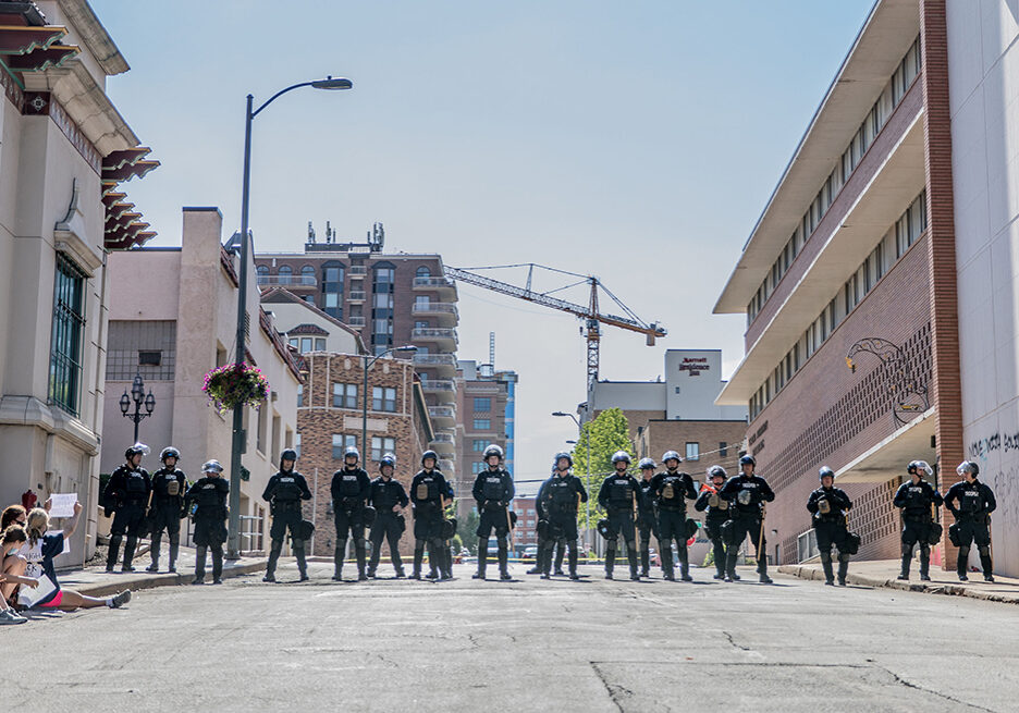 A row of police line up in the middle of the street on the Country Club Plaza, flanked by demonstrators on the left and right.