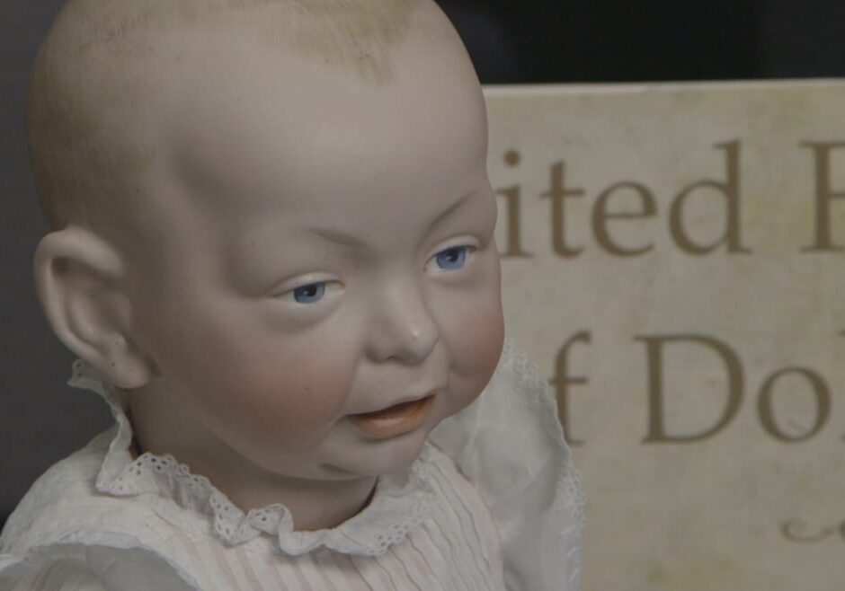 Close-up image of painted bisque baby doll in white linen gown.
