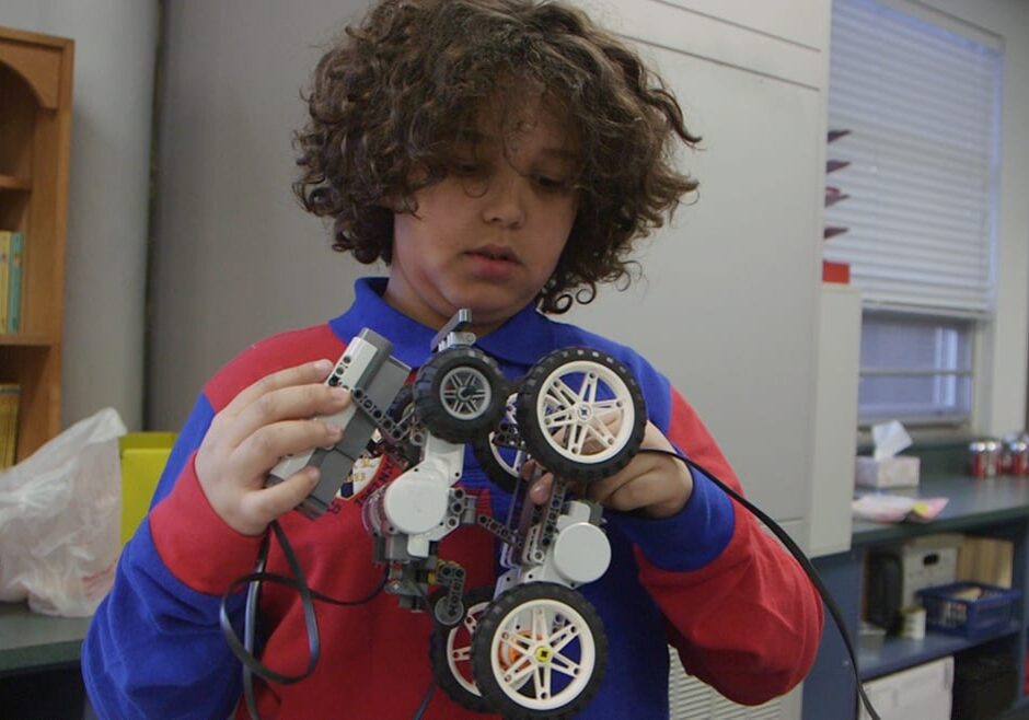 Young boy holding up electrical device with wheels.