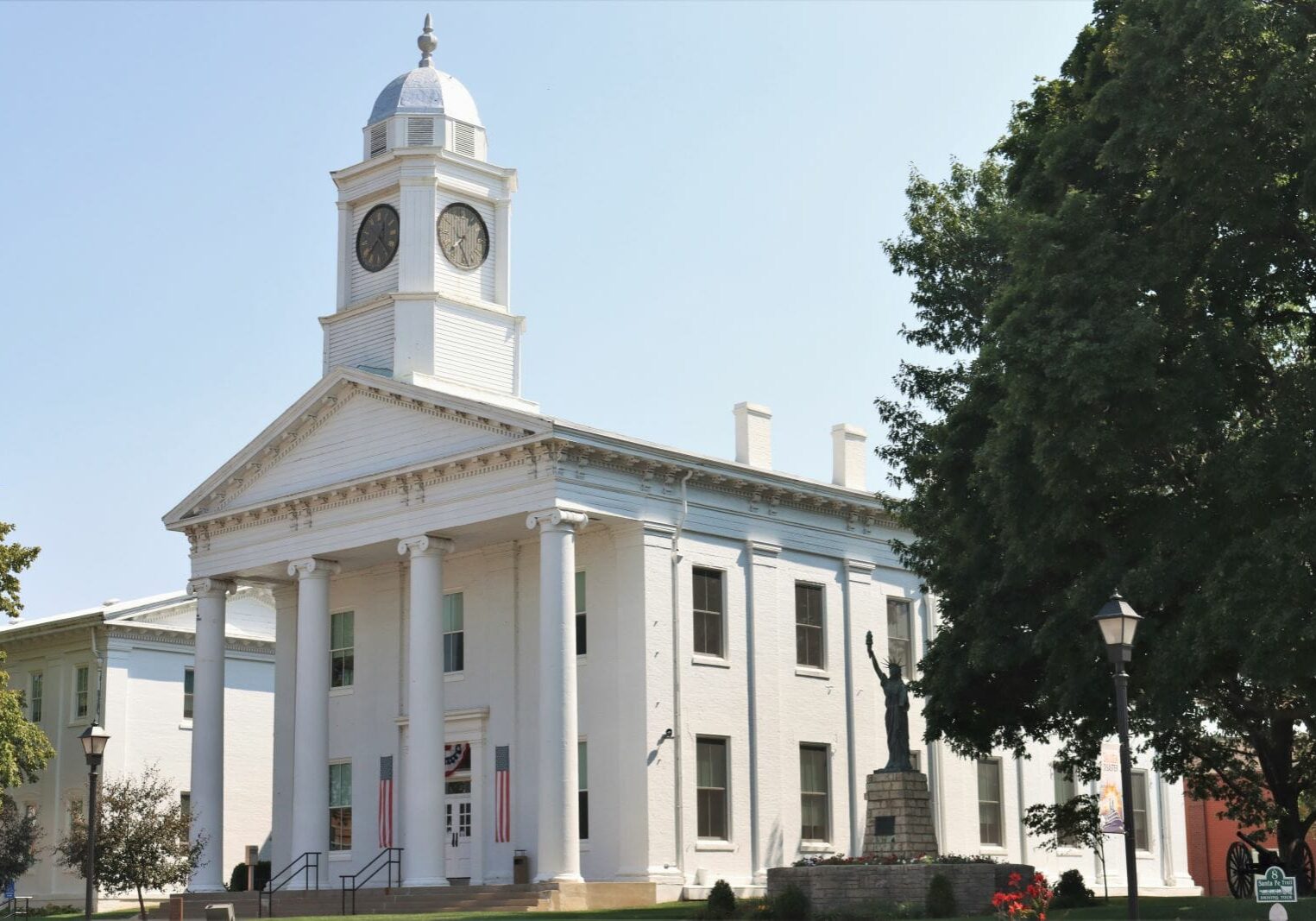 A white courthouse built in the Greek revival style. On top the building is a clock tower.