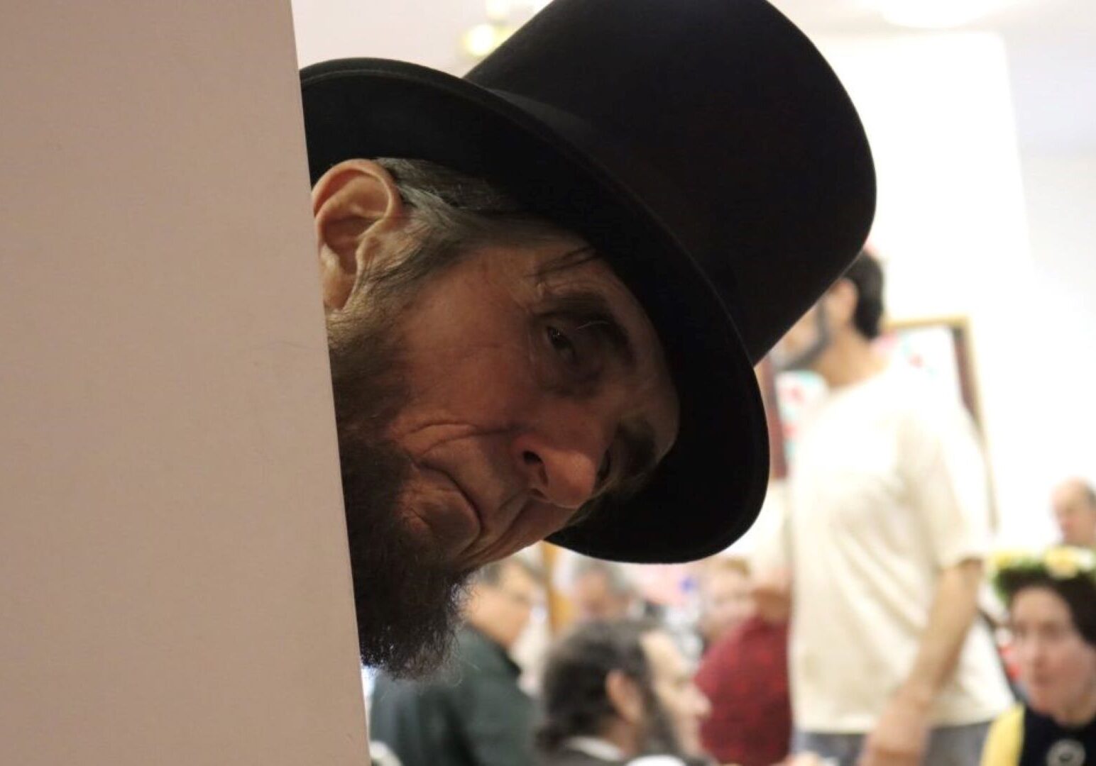 A man dressed as Abraham Lincoln peaks around a wall.