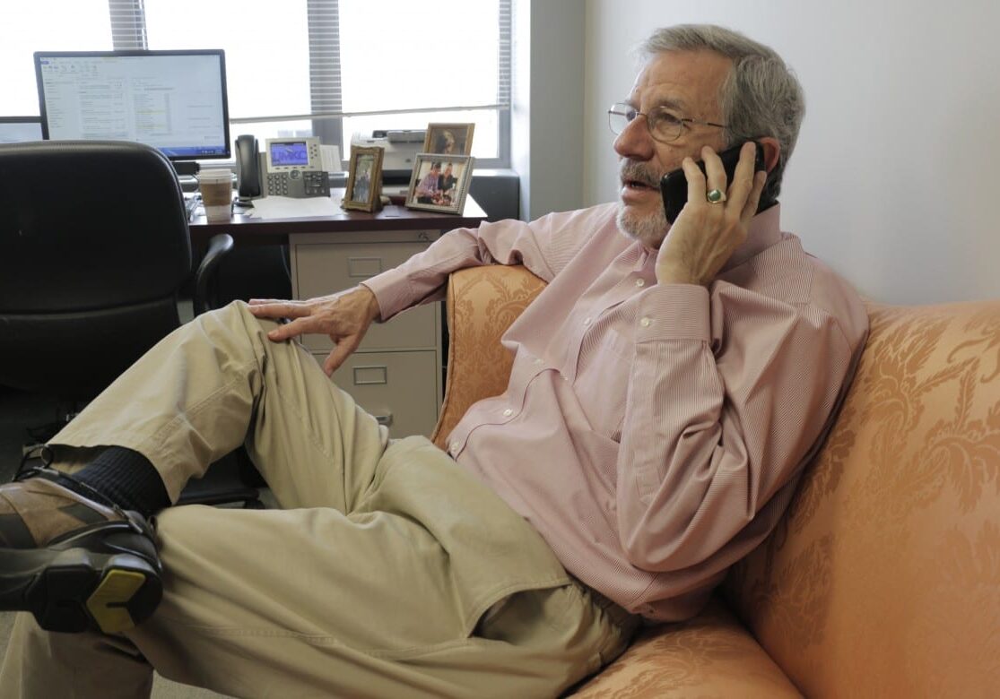 Man sitting on the couch in an office, talking on the phone.