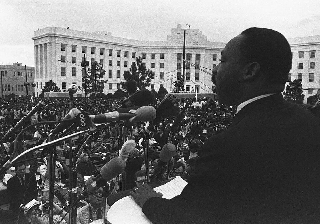 Black and white photo of MLK in front of large crowd.