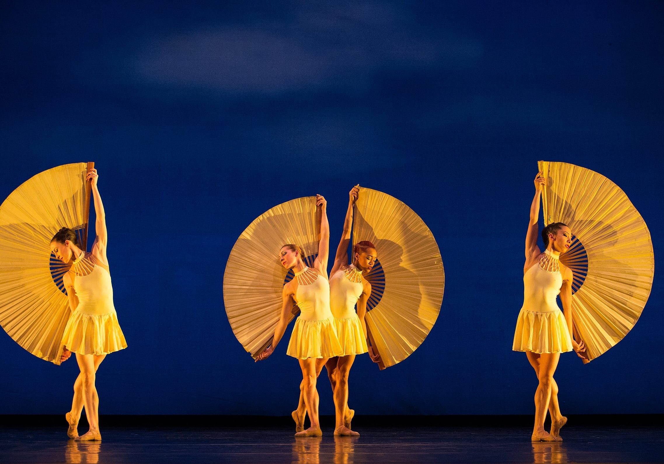 Four women in yellow costume posing against a blue backdrop.