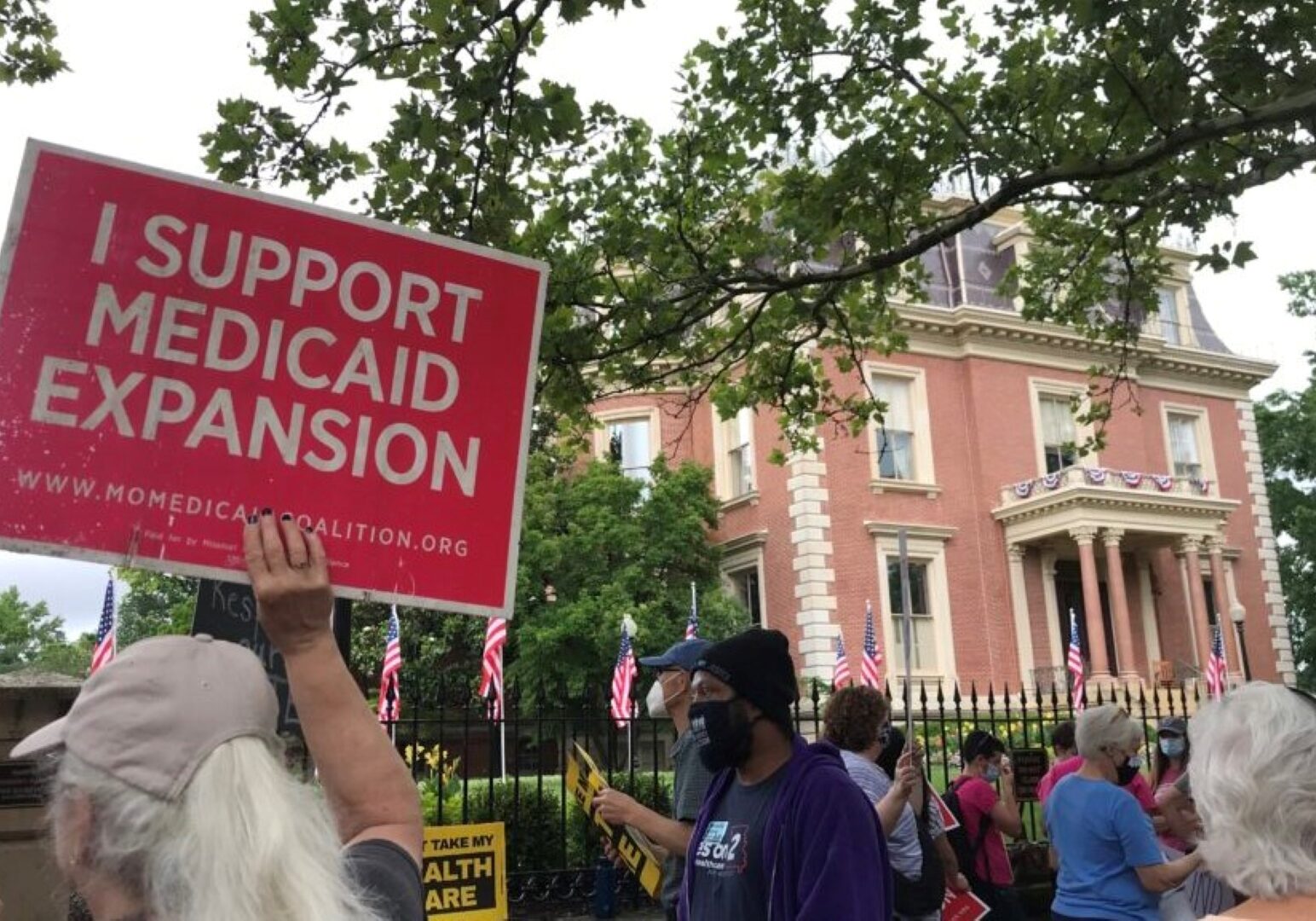 Demonstrators stand outside of the Governor’s Mansion in Jefferson City on July 1, 2021 and hold signs urging Gov. Mike Parson to fund voter-approved Medicaid expansion.
