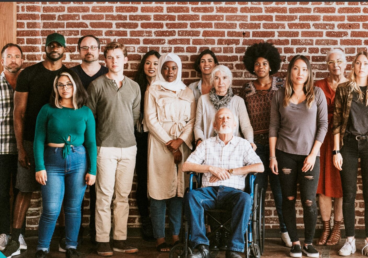 Fourteen people posing in front of a brick wall.