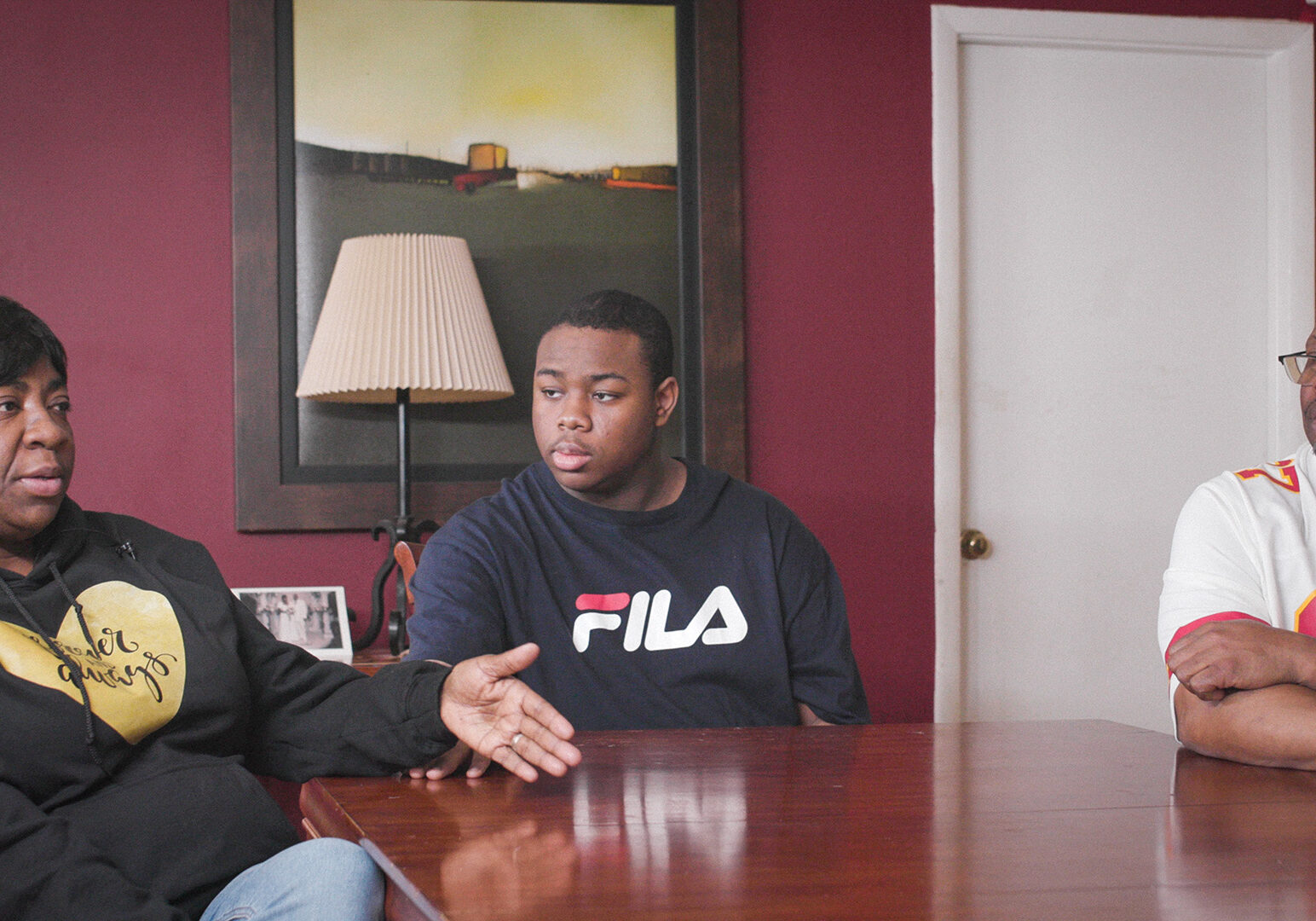 The Mitchell family sits around their kitchen table. Michelle is seated next to 17-year-old son with autism, explaining what she faces juggling work and finding support for her son.