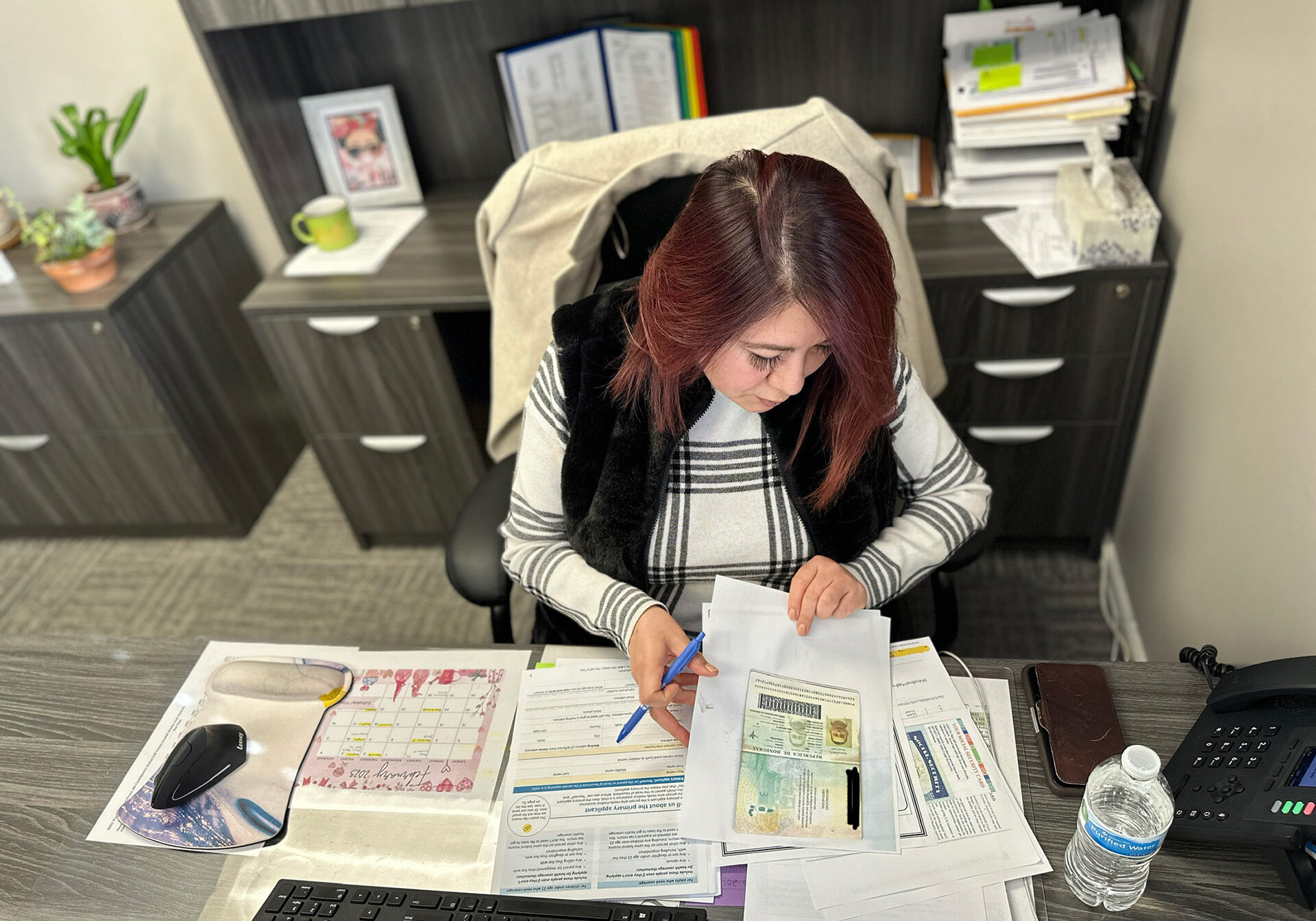 A woman with papers scattered around her on her desk. Ivonne Montanez is a health navigator at El Centro. Here she prepares one of her clients' Medicaid applications. (Vicky Diaz-Camacho | Flatland)