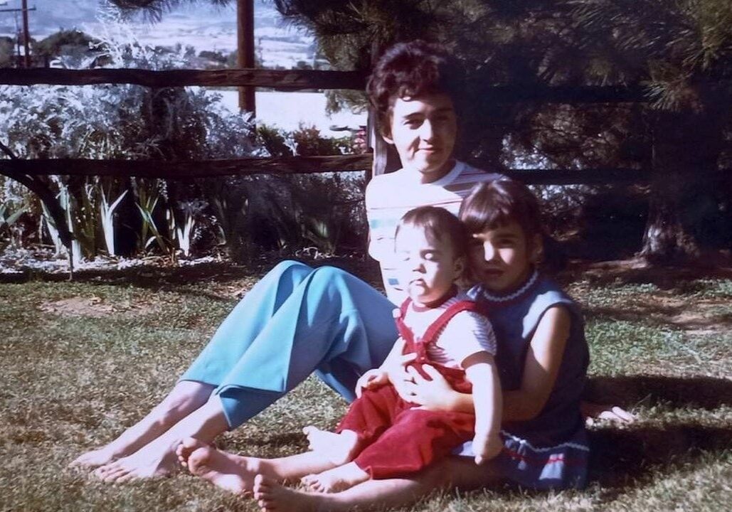 A mother and two children sitting in the grass.