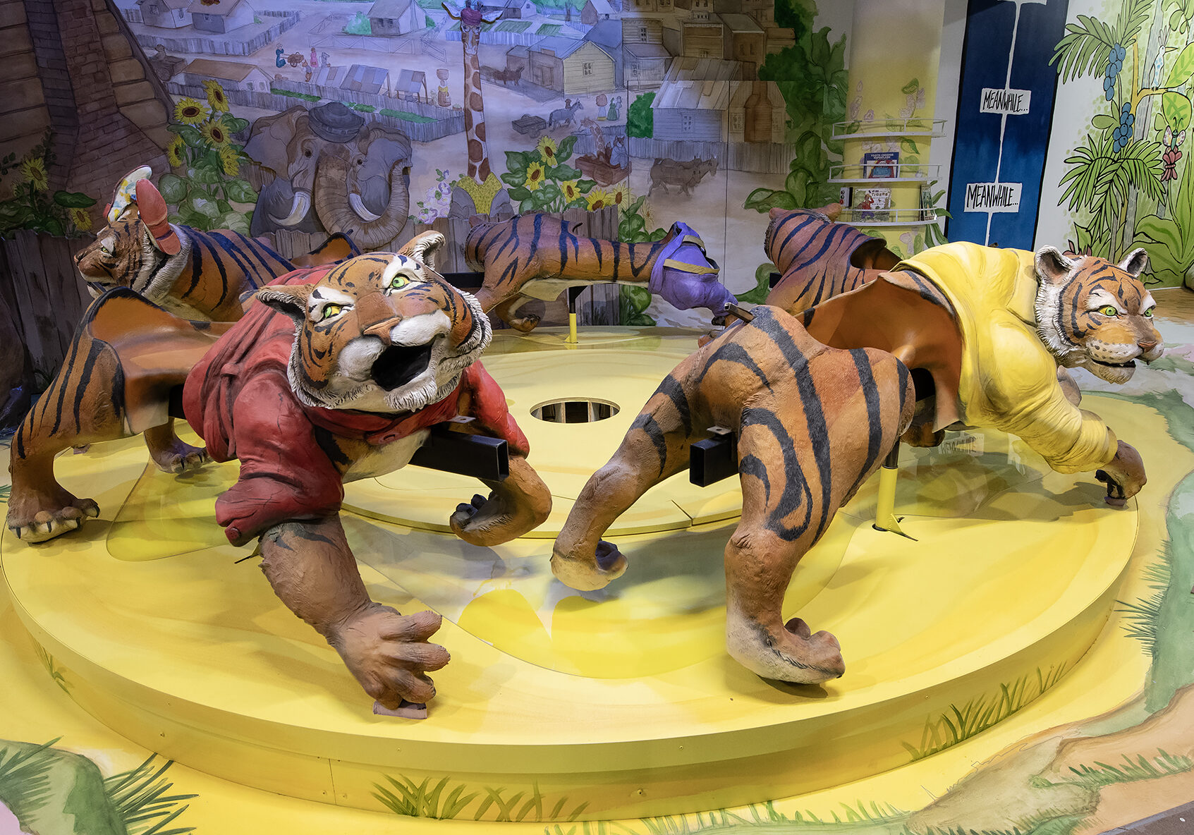 A colorful merry-go-round with tigers in an exhibit still in progress based on “Sam and the Tigers,” the book by Julius Lester. Each exhibit includes bookshelves.