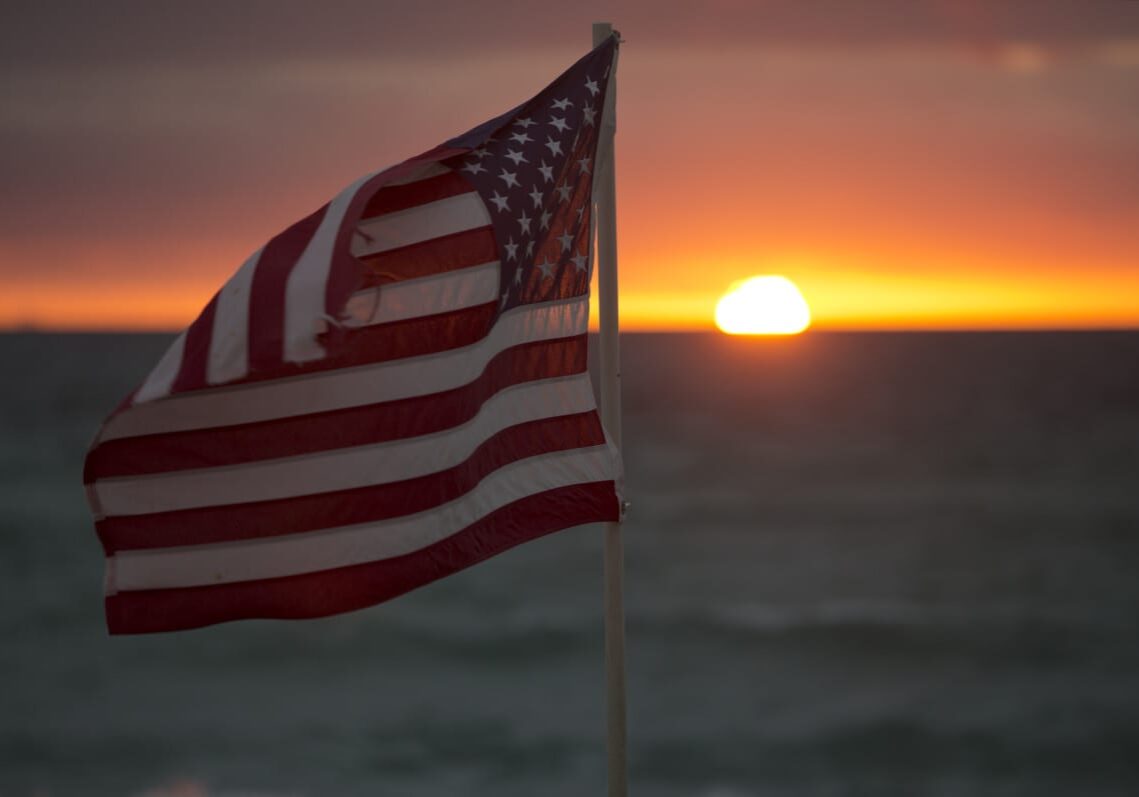 The flag of the United States is set against a sunset.