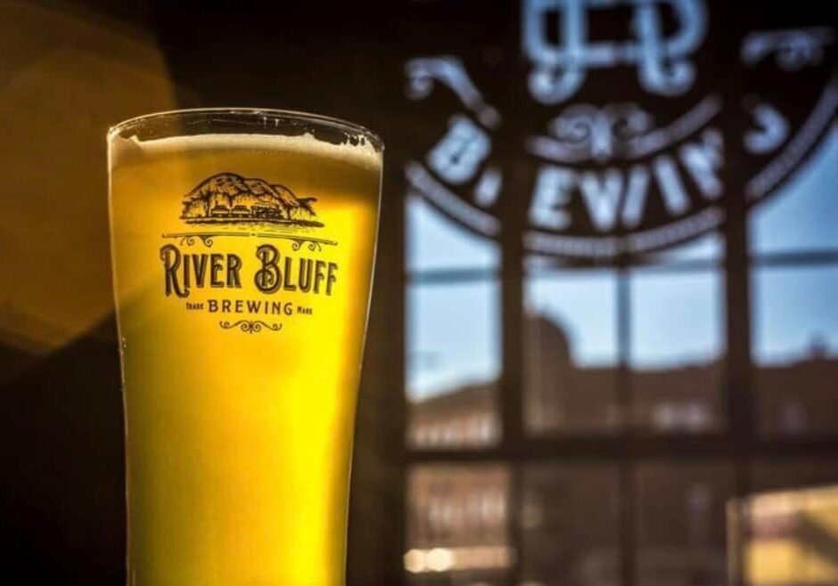 River Bluff Brewing beer in a glass in front of a window.