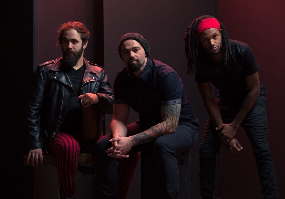 Three men in a band sit in a dark room.