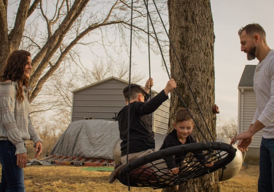 Woman and man push two young boys on a rope swing.