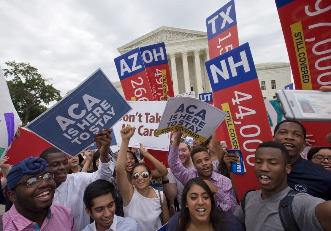 Students cheer as they hold up signs stating that numbers of people in different states who would lose healthcare coverage, with the words "lose healthcare" now over written with "still covered" stickers, after the Supreme Court decided that the Affordable Care Act may provide nationwide tax subsidies, Thursday June 25, 2015, outside of the Supreme Court in Washington. (AP Photo/Jacquelyn Martin)