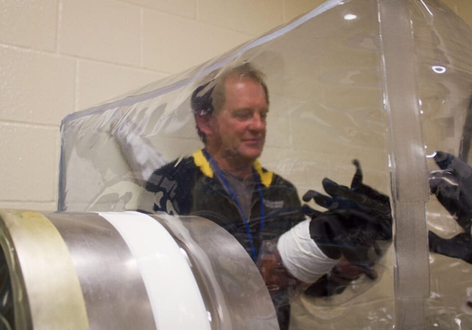 Minnesota veterinarian and researcher Scott Dee, of Pipestone Veterinary Services, fits his hands inside the gloves used to access a germ-free pen. During studies with PEDV, the germ-sealing qualities of the pen were used to keep the virus in, as piglets sampled feed spiked with it. (Photo: Amy Mayer | Harvest Public Media)