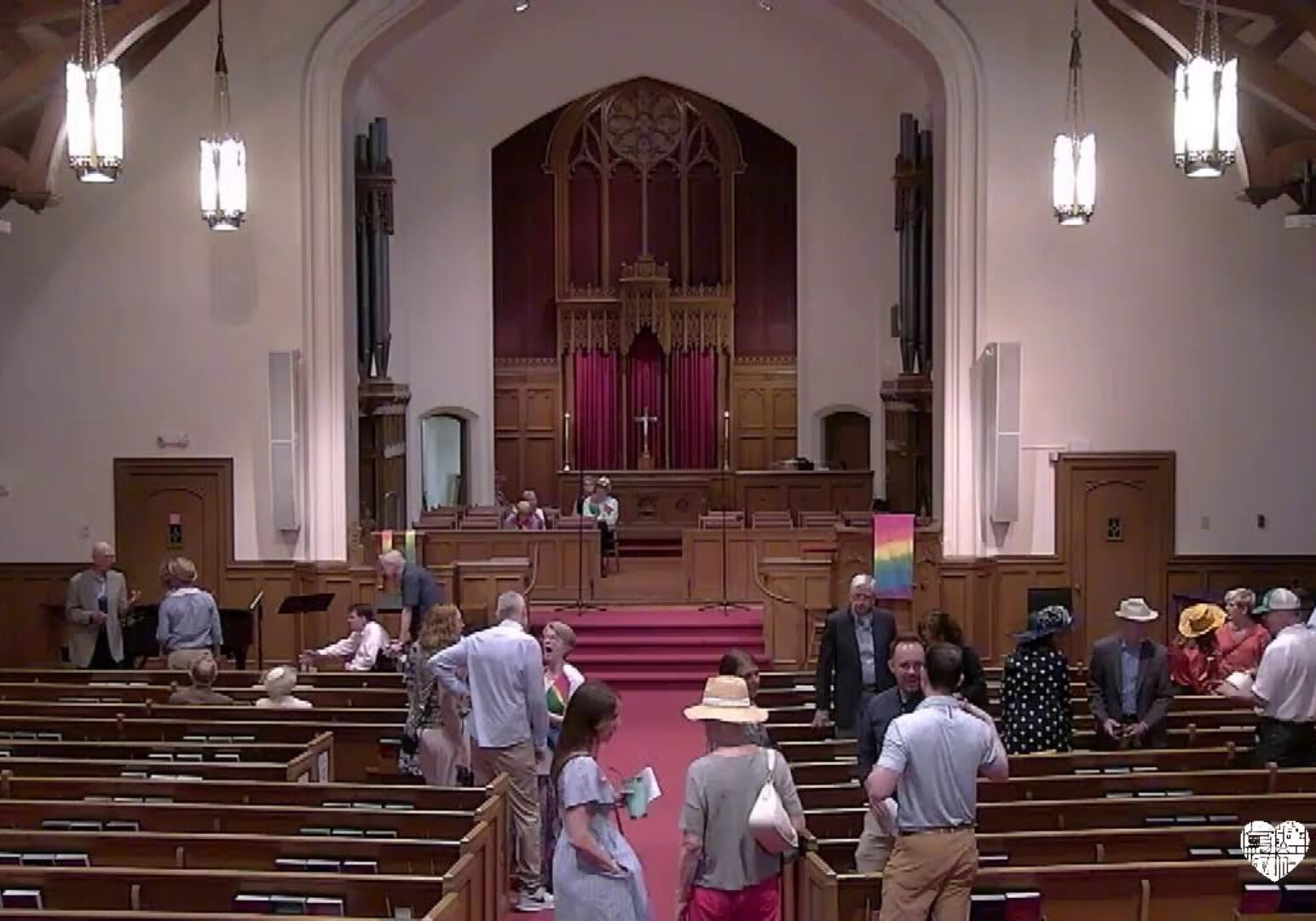 A Sanctuary of a church with people standing in the pews and aisle.