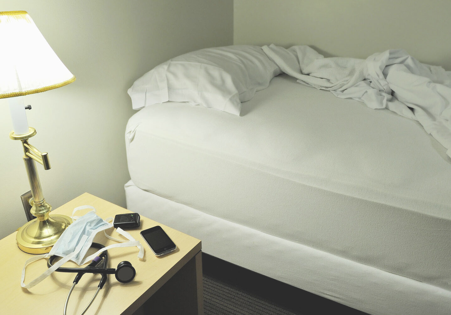 A room in a sleep clinic shows a lamp, a twin bed with white sheets flipped open. On the nightstand is a phone, stethoscope and a mask. The American Psychological Association called sleep disorders an "epidemic." COVID-19 made things worse.