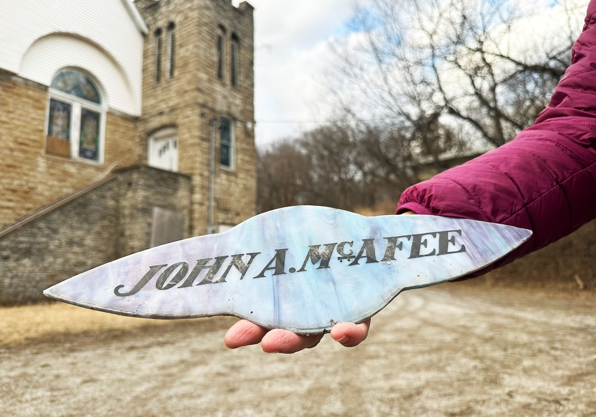 Hand holding a piece of stained glass window with the name John A McAfee on it.