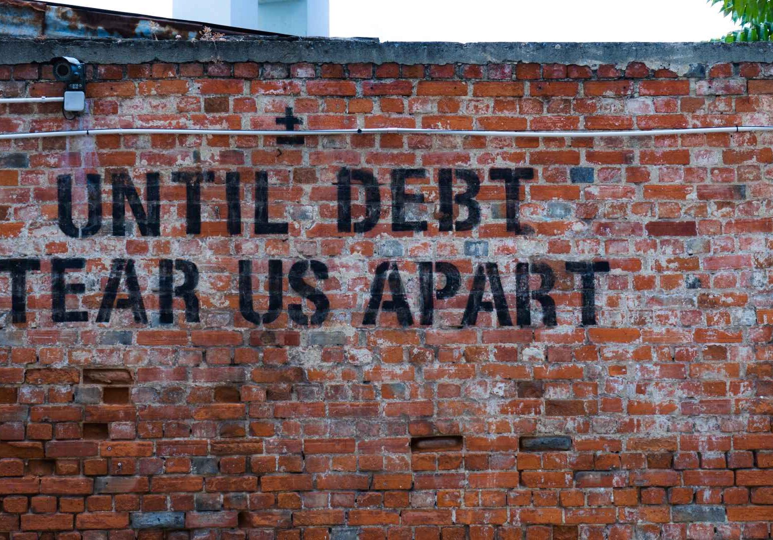 A brick wall painted with the words "Until Debt Tear Us Apart."