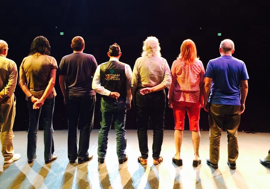 Photo of the backs of seven people standing on a stage.