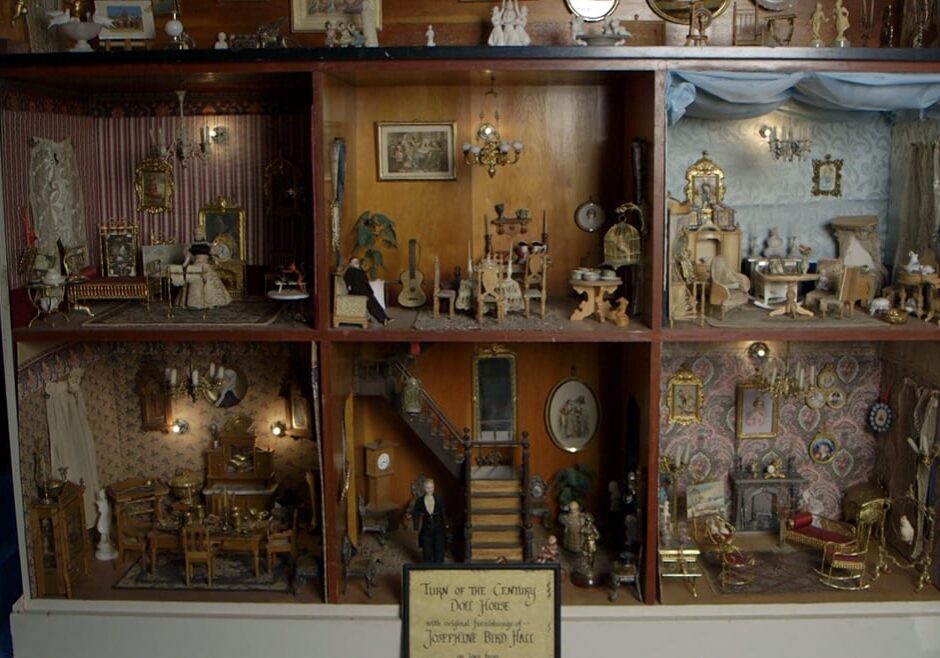 Wide image of Victorian dollhouse with three stories and seven ornately furnished rooms.