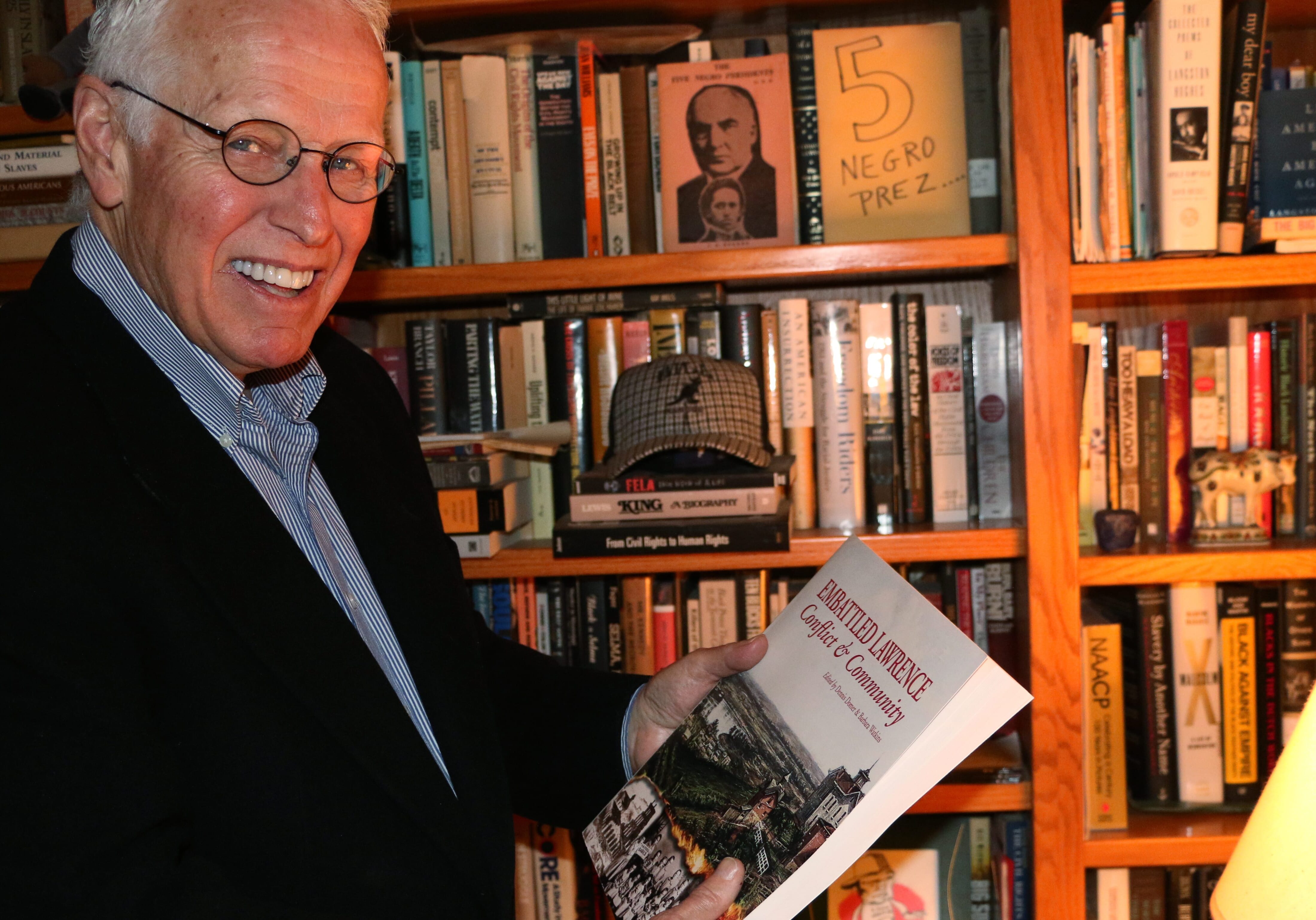 Photo of man holding book in front of bookcase.