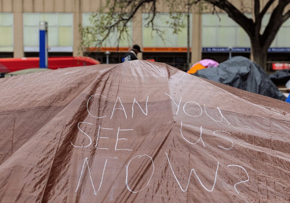 A hand drawn sign appears on a tarp covering tents at the Kansas City Homeless Union’s City Hall occupation on April 7.