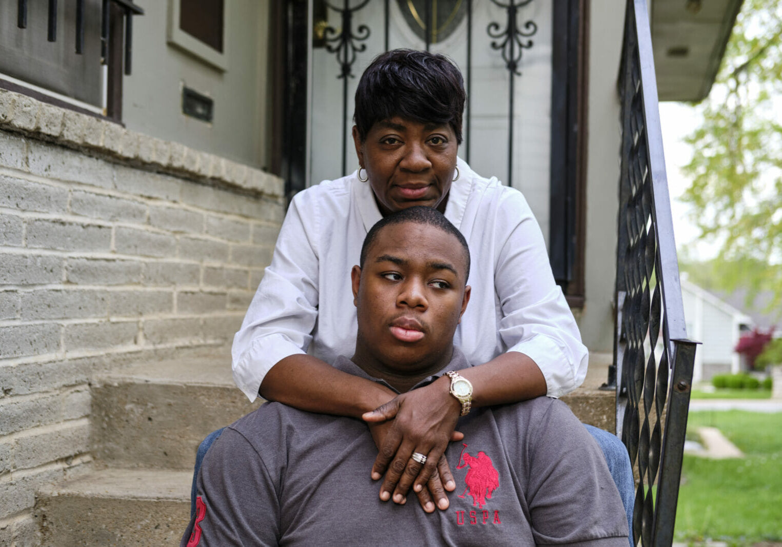 A Black mother with short hair and a white blouse crosses her arms around her 17-year old son who has autism. Michelle Mitchell worries about the small things in life, like sending Gerald to a bus stop. The bigger things, like career, are even more dizzying. (Dominick Williams | Flatland)