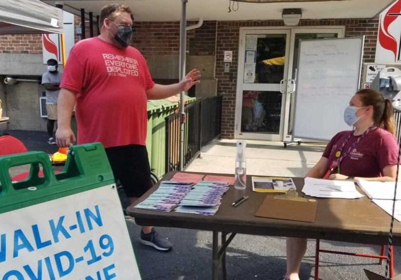 Mark Kirchhoff, left, a volunteer with Columbia Project Homeless Connect, speaks July 29, 2021 with Taylor Knoth, a public health nurse, at the registration table for a COVID-19 vaccination clinic.