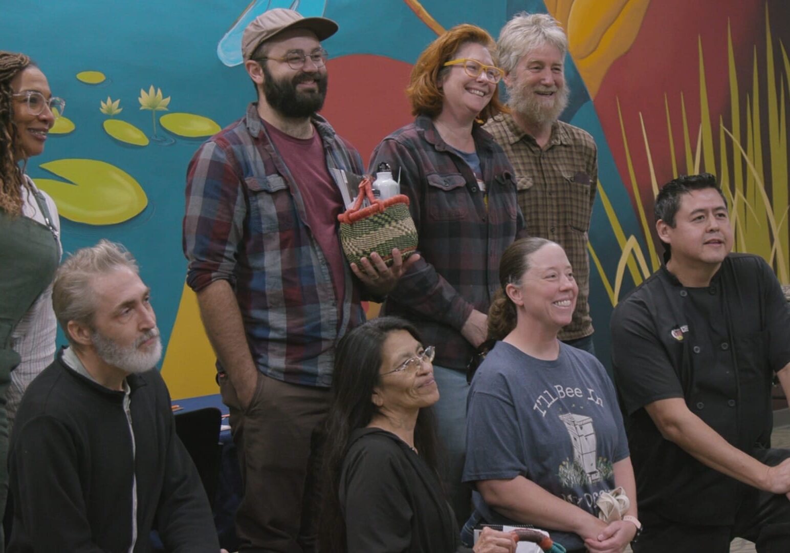 Folks pose for a photo while holding baskets of goodies in front of a colorful mural.