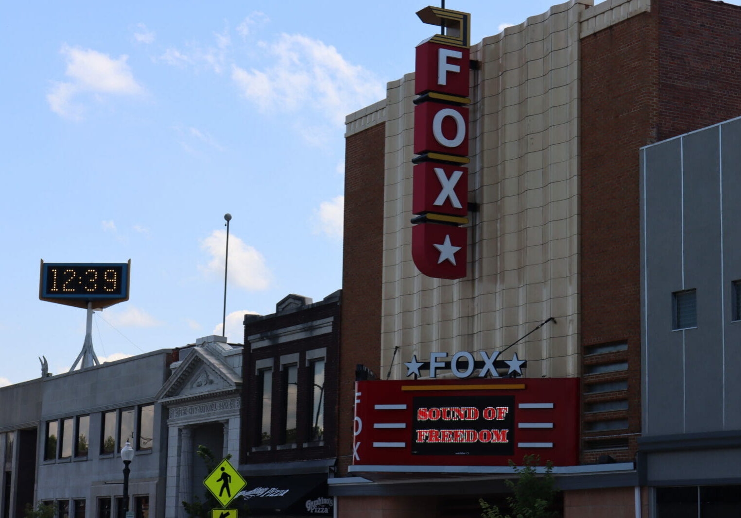 A vertical sign on a tall brick and white stone building reads "FOX" lower down a digital marquee reads "Sound of freedom"
