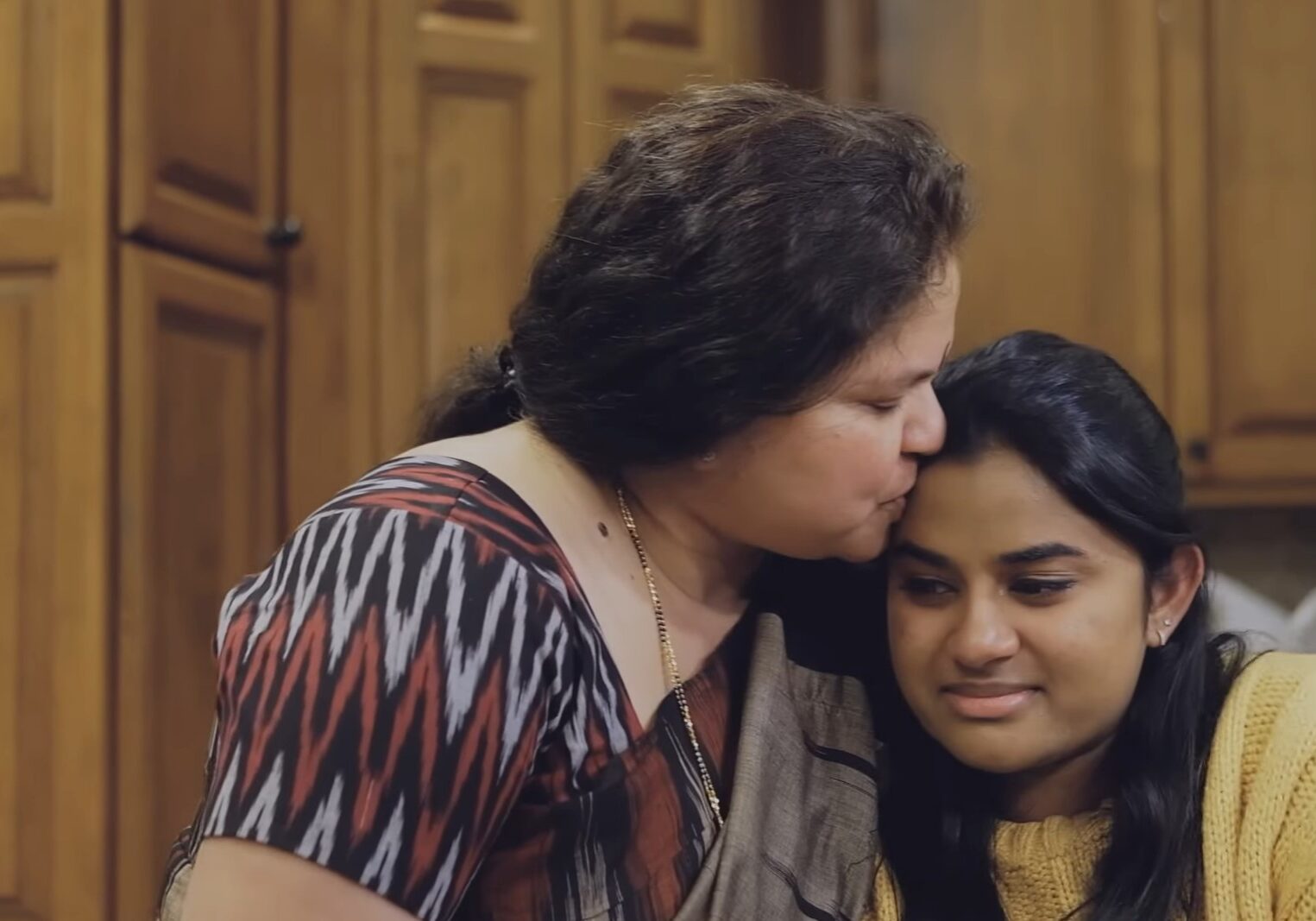 A mother kisses her daughter on the forehead. The daughter is crying,