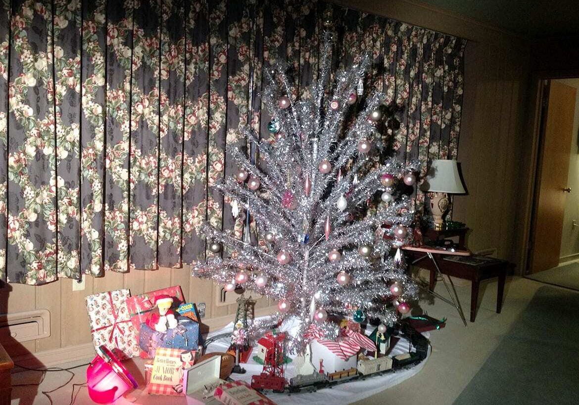 Aluminum Christmas Tree illuminated by a rotating color-wheel in 1950s looking living room with 1950s era present under the tree.