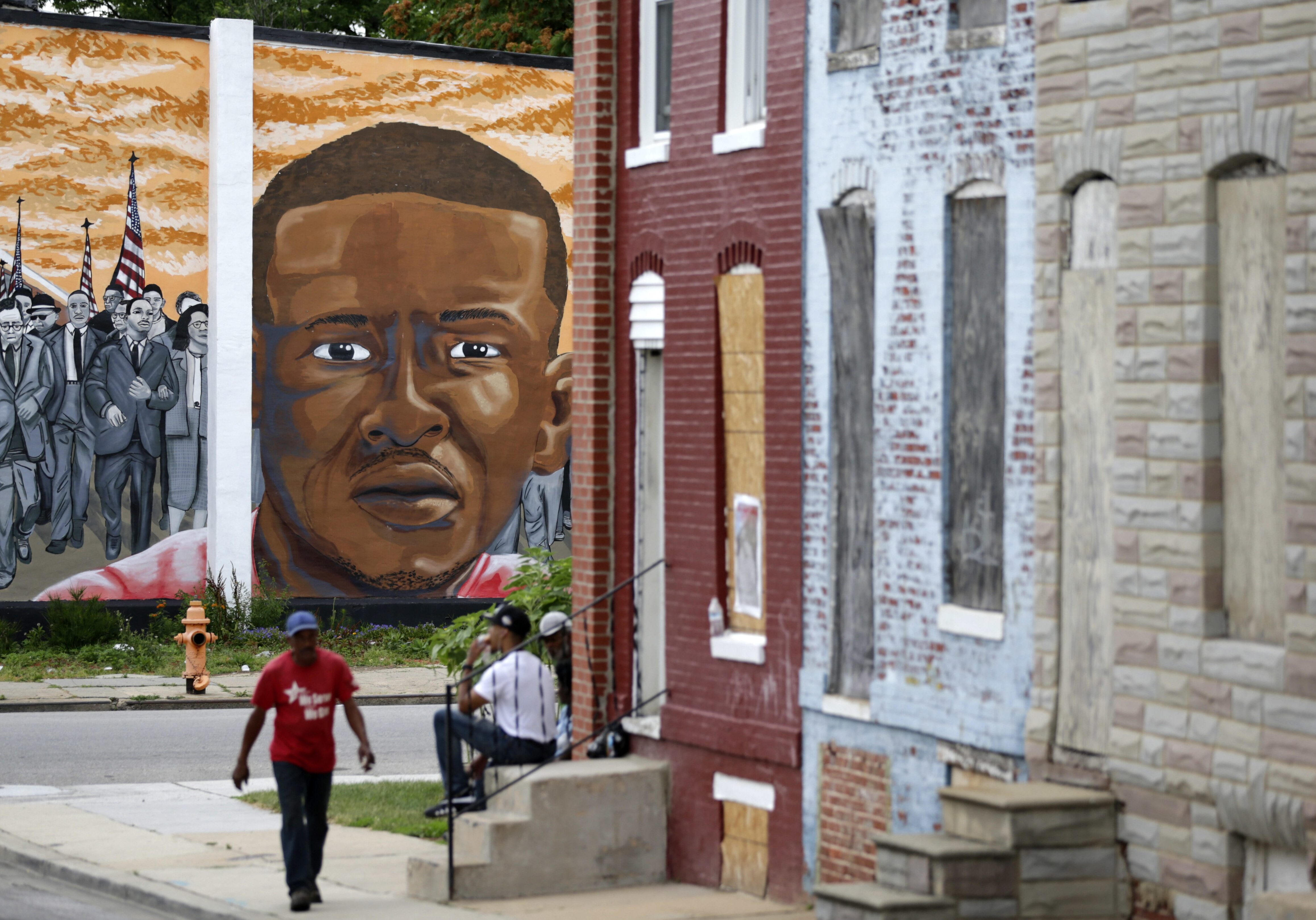People walk by a mural depicting Freddie Gray in Baltimore on June 23, at the intersection where Gray was arrested in 2015.