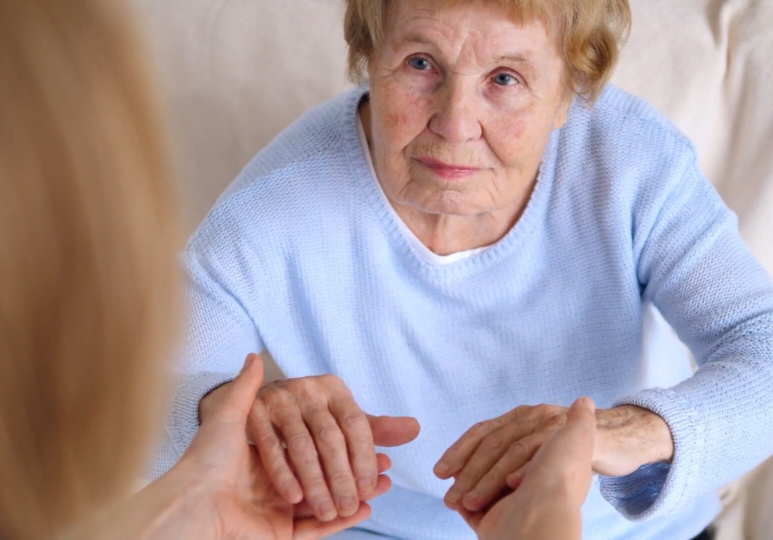 Elderly woman holding hands with unseen caregiver