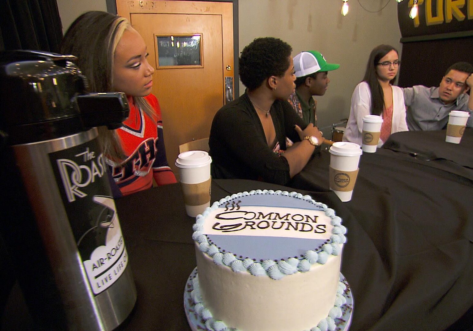 Teens sit at a table with a cake and coffee.