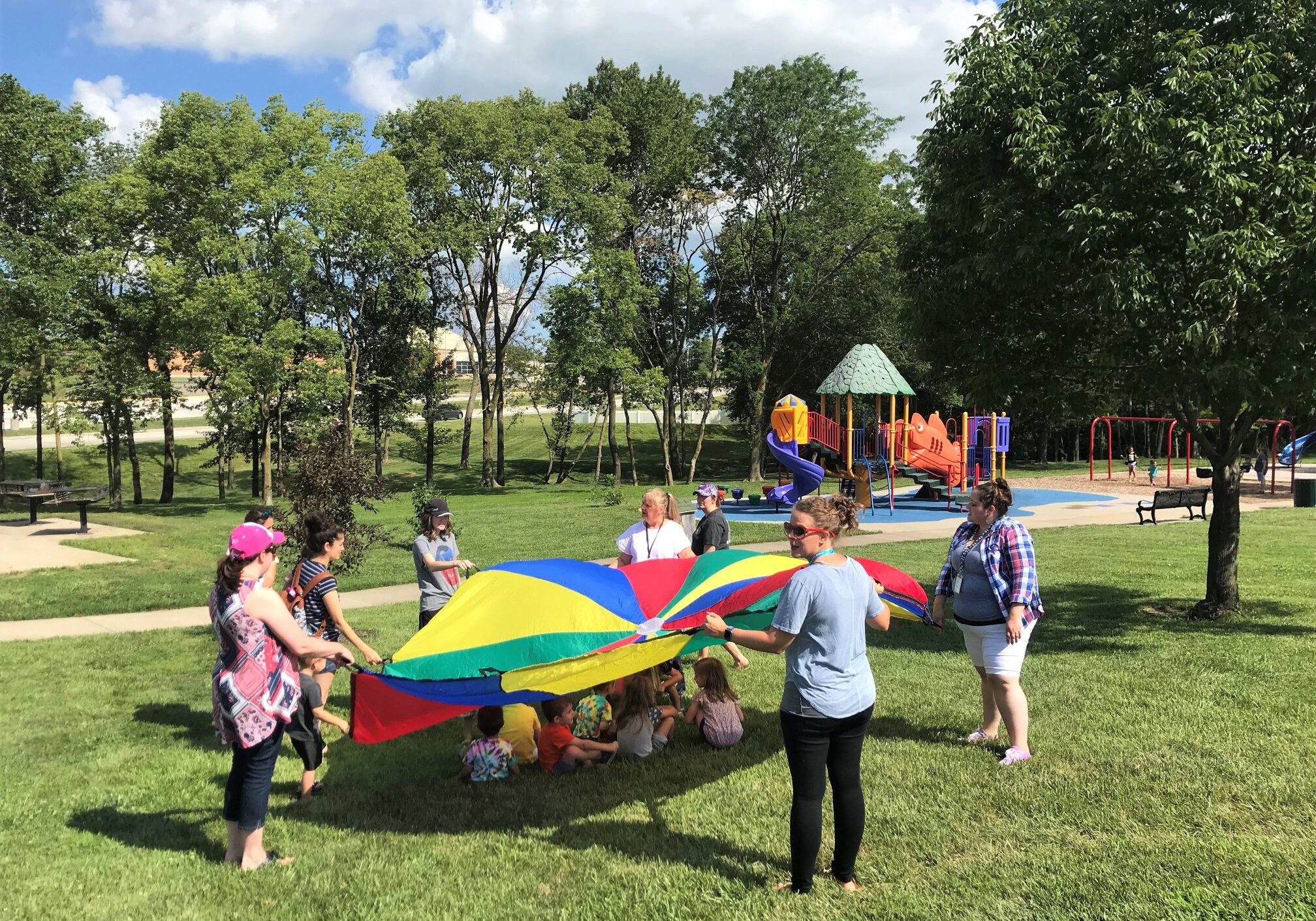 staff and children at summer camp activity under a parachute at a park