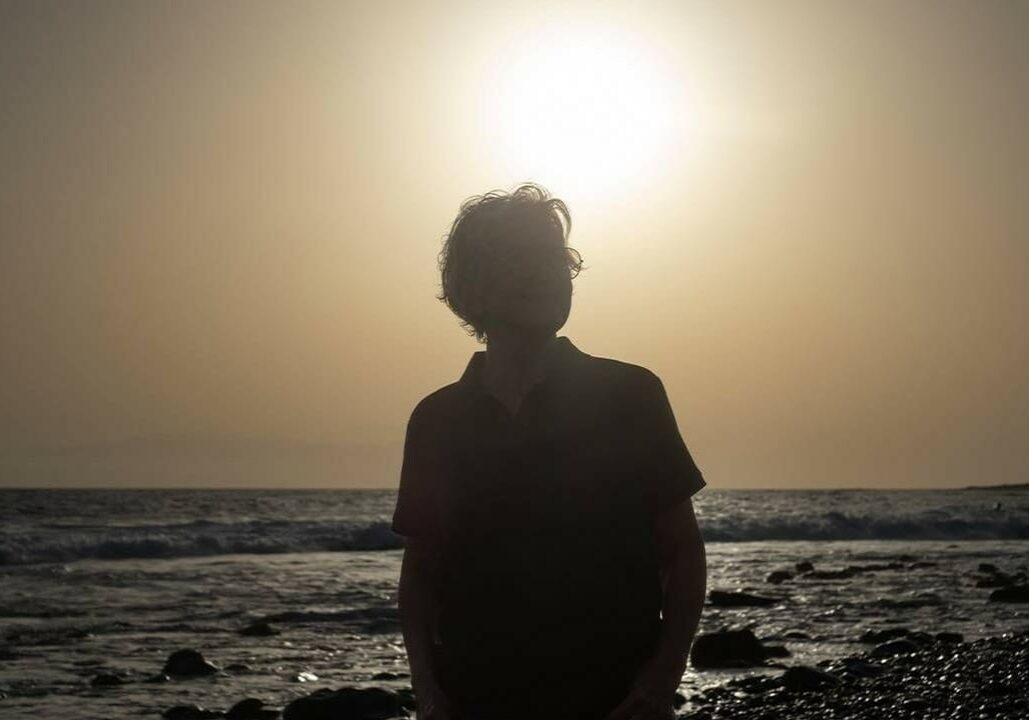 A woman walking on a beach with the sun setting behind her.