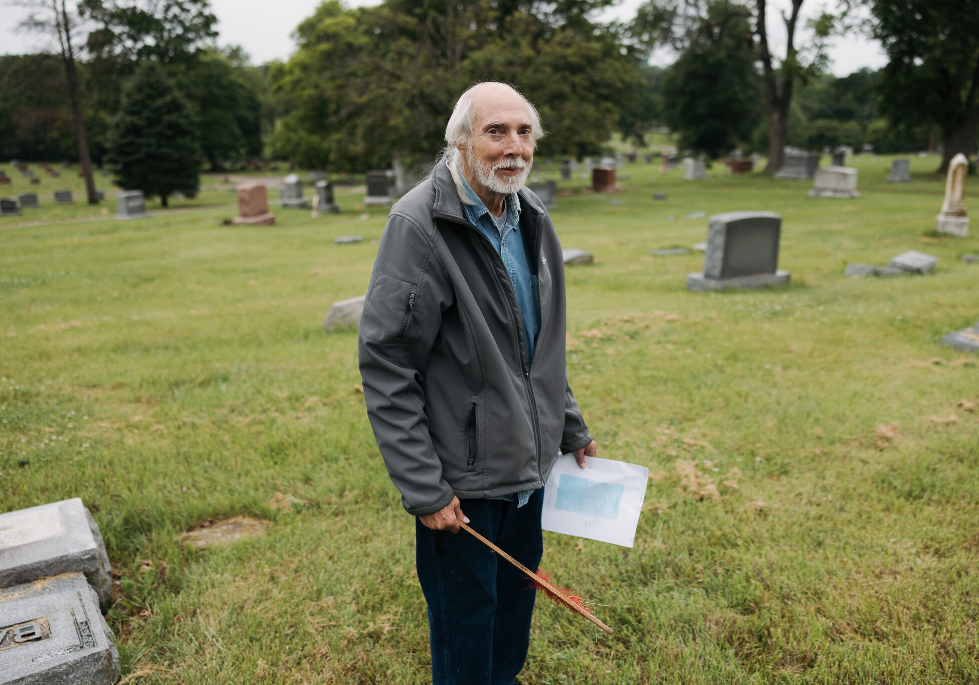 Robert Franke stands for a photo with a map and a brush for clearing gravestones at Forest Hill Cemetery, off Troost in Kansas City, Missouri. Franke gathers users’ search requests at findagrave.com to generate a list of names and info he uses to locate the grave sites. (Chase Castor | Flatland