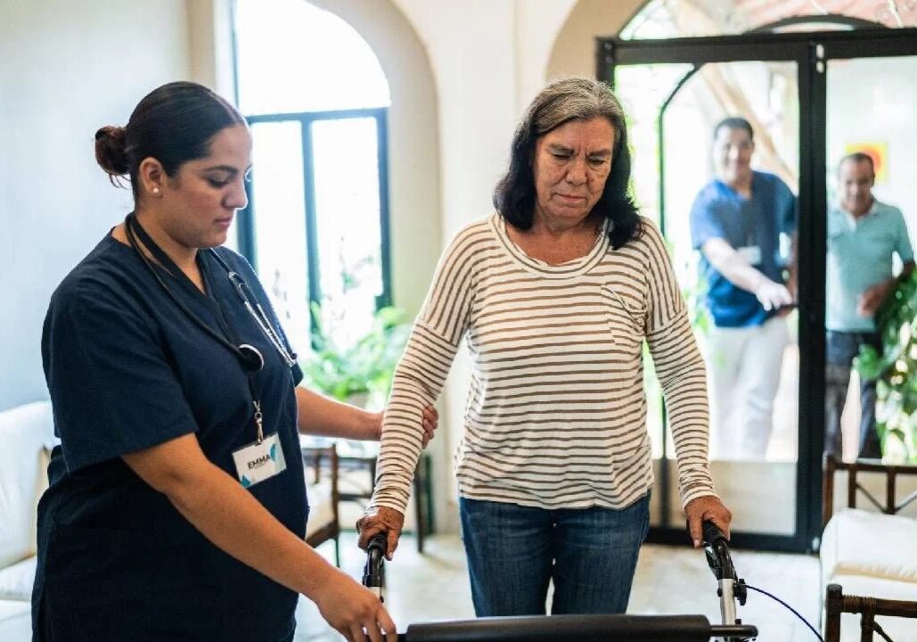 A nurse assists a woman using a walker.
