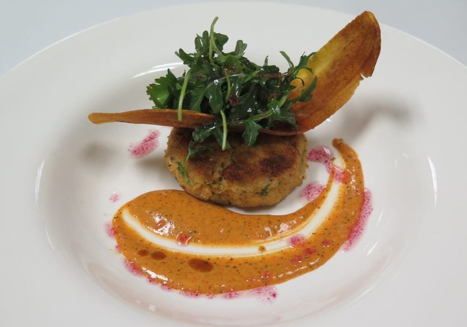 A crab cake with a chip and sauce.