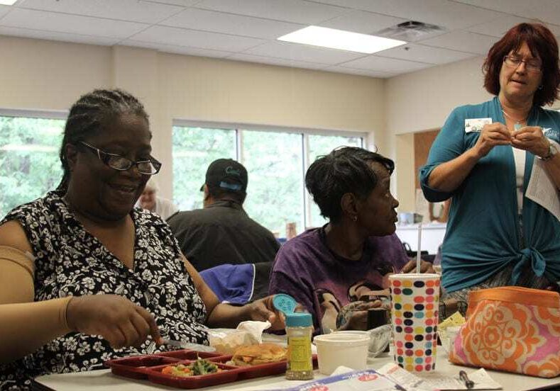 Marian Kennedy, left, and Ollie McCregg, both of Topeka, have lunch at Midland Care's PACE Center. PACE, which stands for Program of All-Inclusive Care for the Elderly, provides wraparound services - mental, physical and emotional - for low-income people with complex medical needs. Midland also provides hospice services and has extended its palliative care to clients in both programs. Roberta Stauffer, right, is the PACE program's adult day coordinator. Photo by Mike Shields.