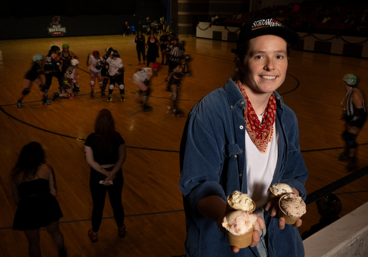 With a roller derby bout underway, Zoe Mays of Scream Queens vegan ice cream, a resident concession partner at the event, posed with the four special flavors she developed in partnership with the teams. The Kansas City Roller Warriors bout was at Memorial Hall in Kansas City, Kansas on Dec. 6, 2025. (Todd Feeback | Flatland)