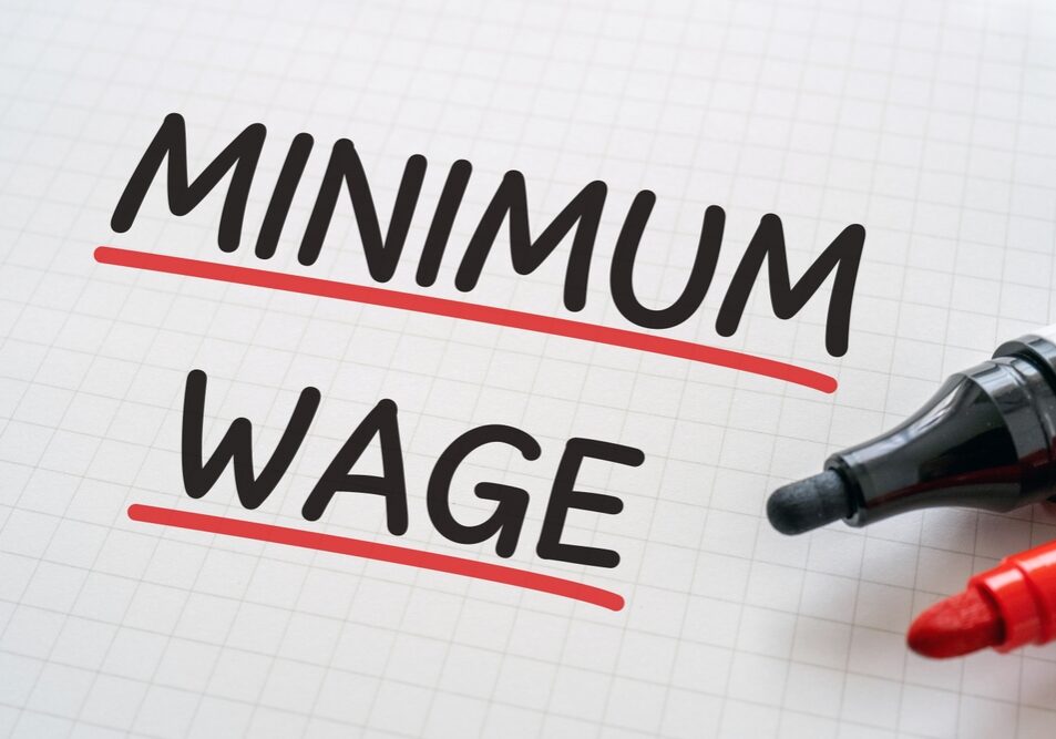 The words Minimum Wage are written in black ink with red underlines on a piece of graph paper with a red and black marker sits next to them on the page.